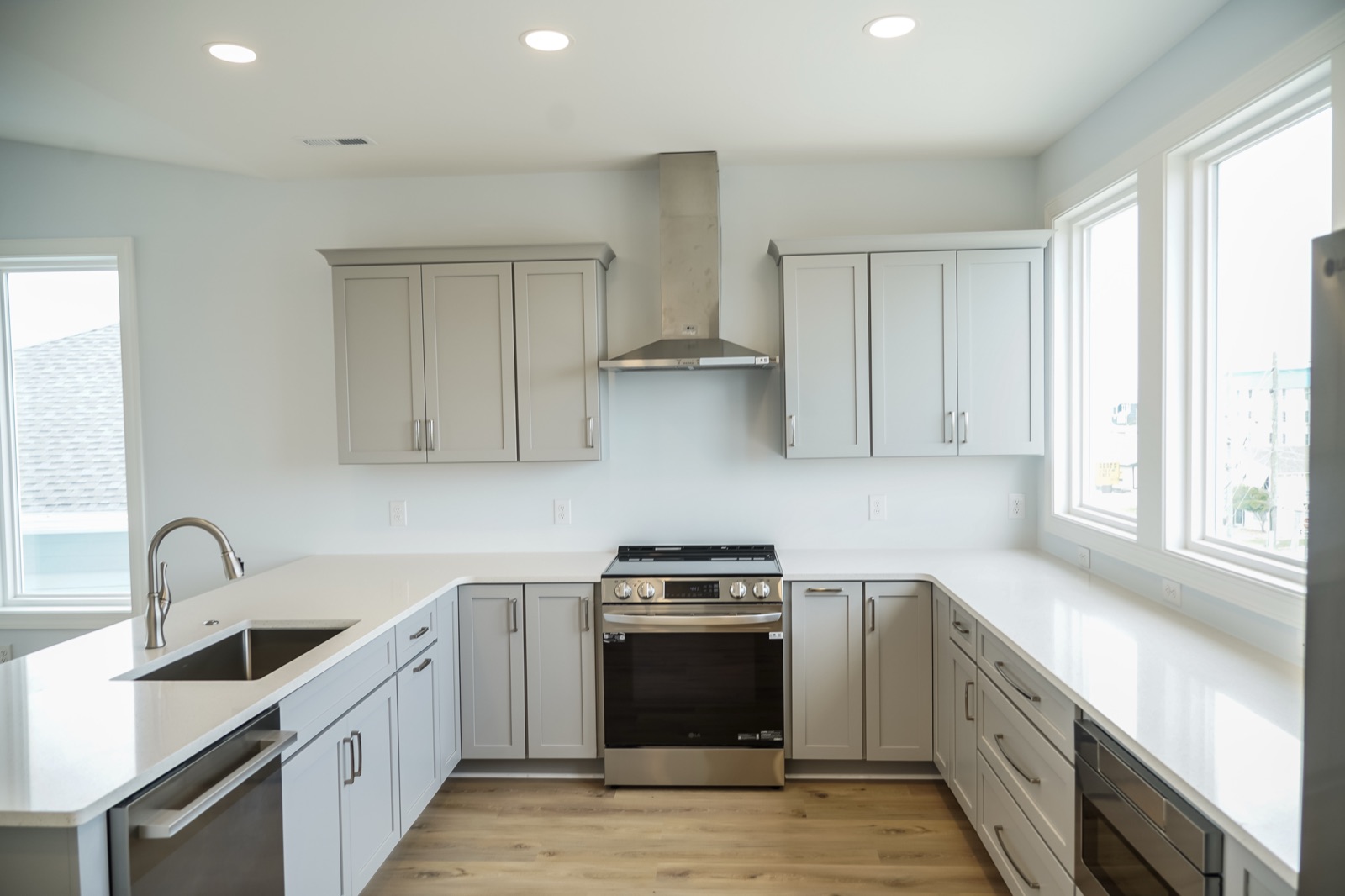 Grey shaker cabinets around a stainless range hood by Shoreline Cabinet Company, Wilmington NC