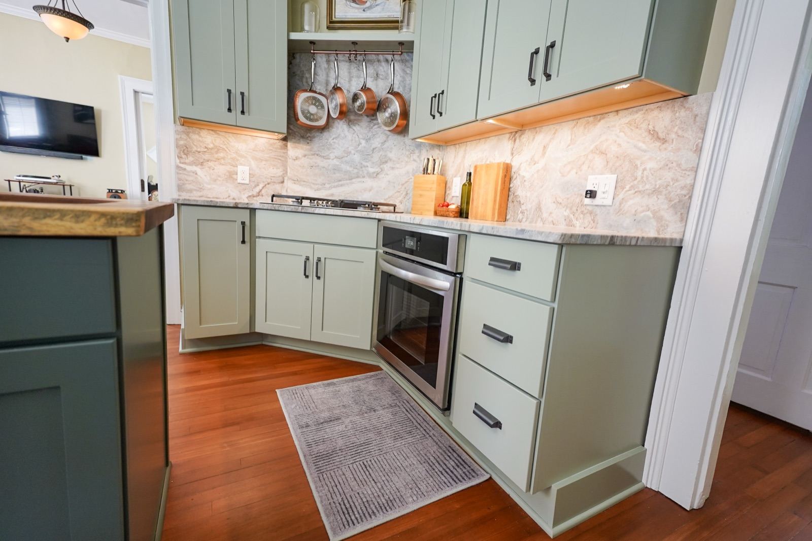 Marble slab backsplash with a pot rail under sage cabinets by Shoreline Cabinet Company, Wilmington NC