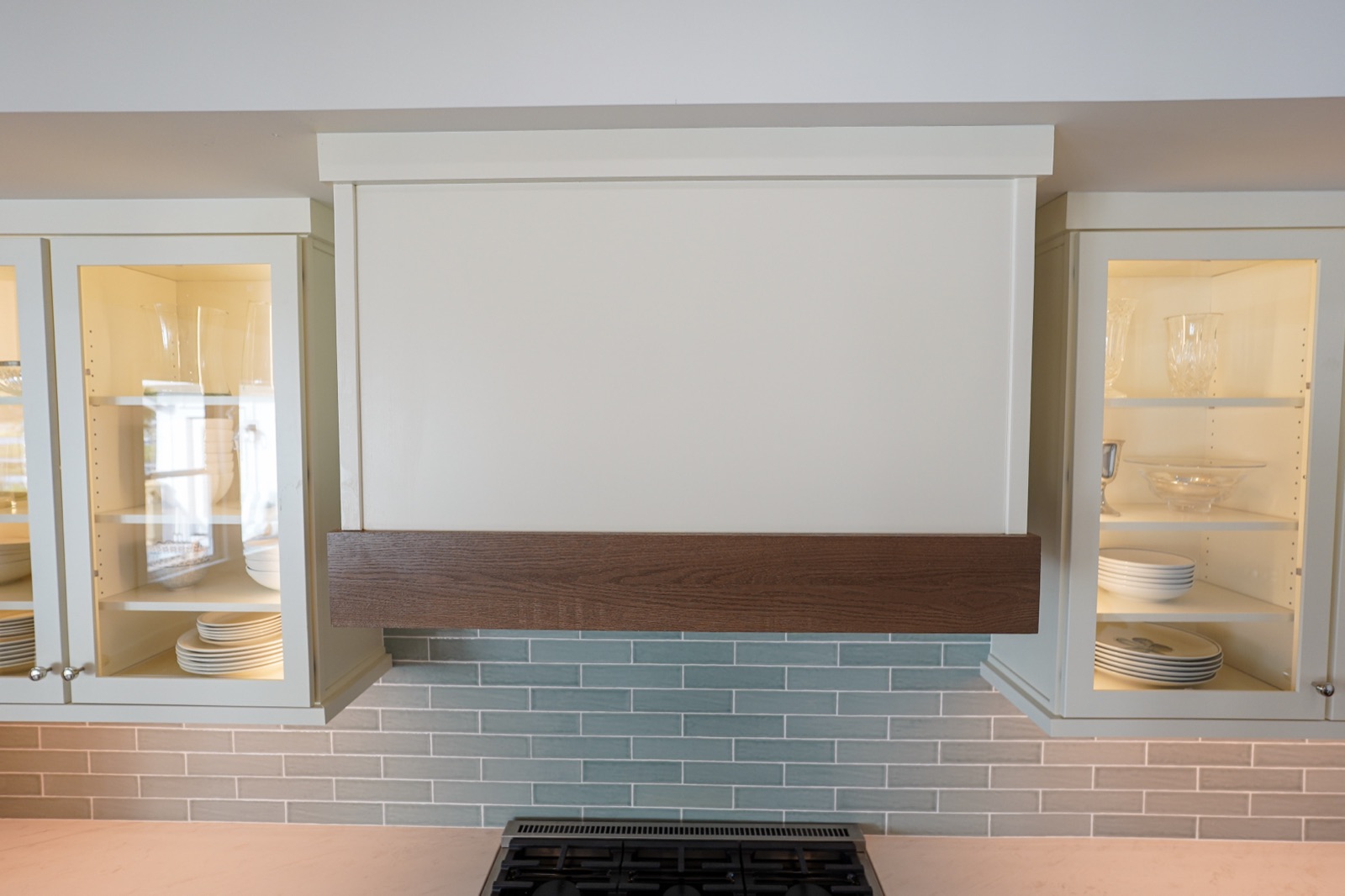 Painted range hood between lit glass-front cabinets by Shoreline Cabinet Company, Wilmington NC