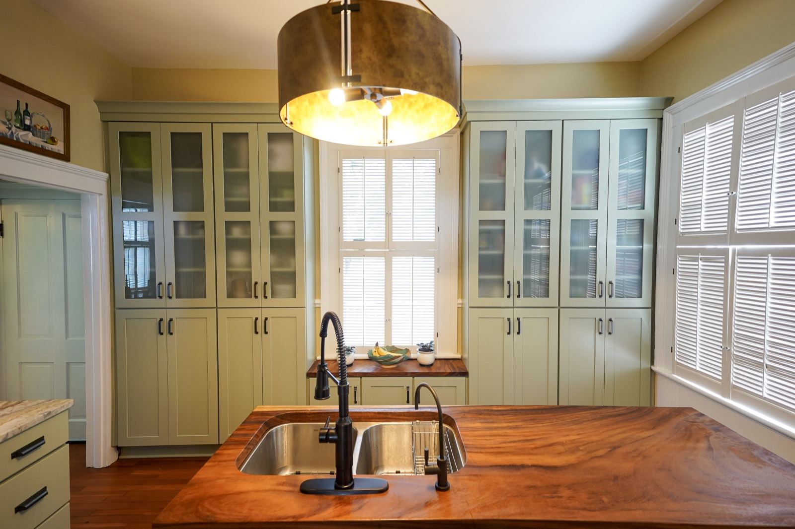 Sage green kitchen with glass-front hutches and a live-edge wood island by Shoreline Cabinet Company, Wilmington NC