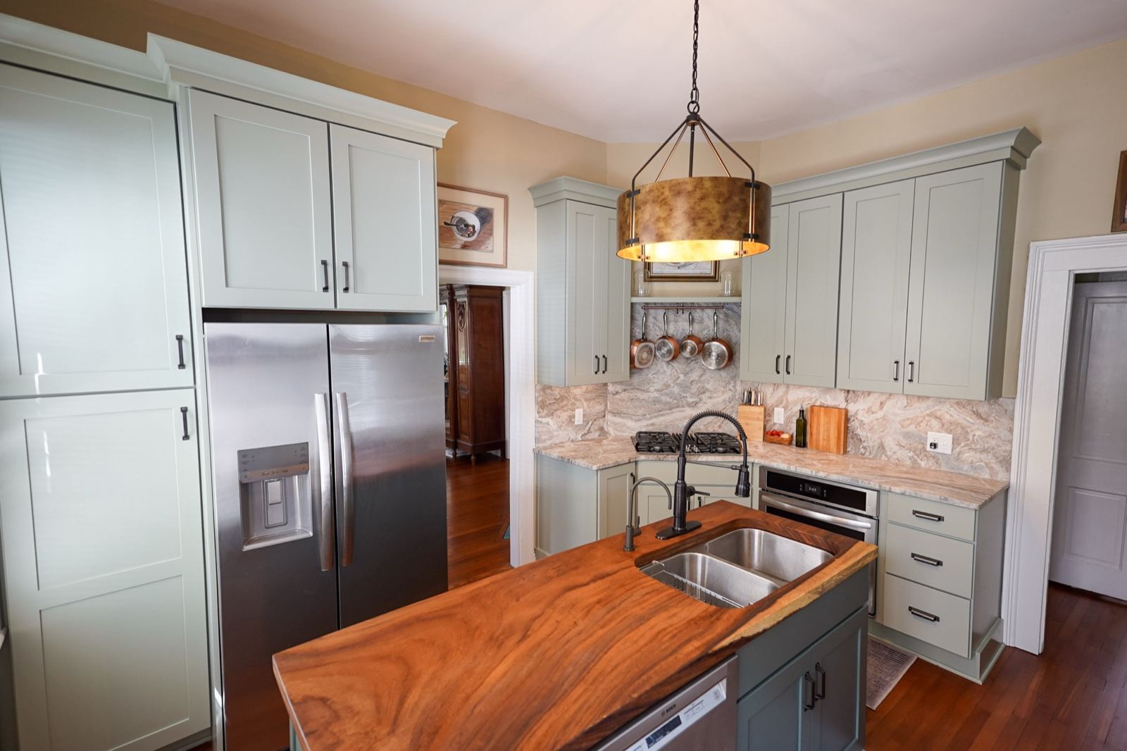 Sage green painted kitchen with a stained wood island, built by Shoreline Cabinet Company in Wilmington, NC