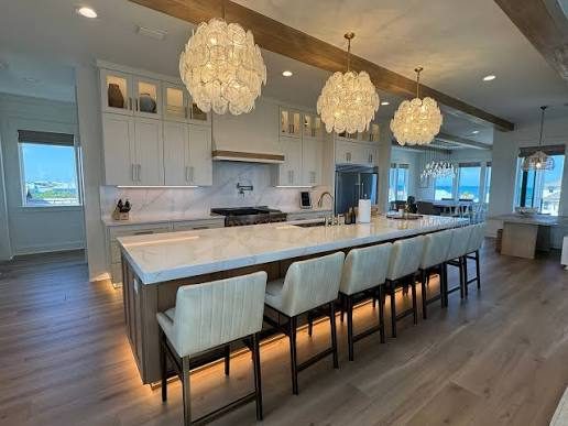 White kitchen with a long seated island under shell chandeliers by Shoreline Cabinet Company, Wilmington NC
